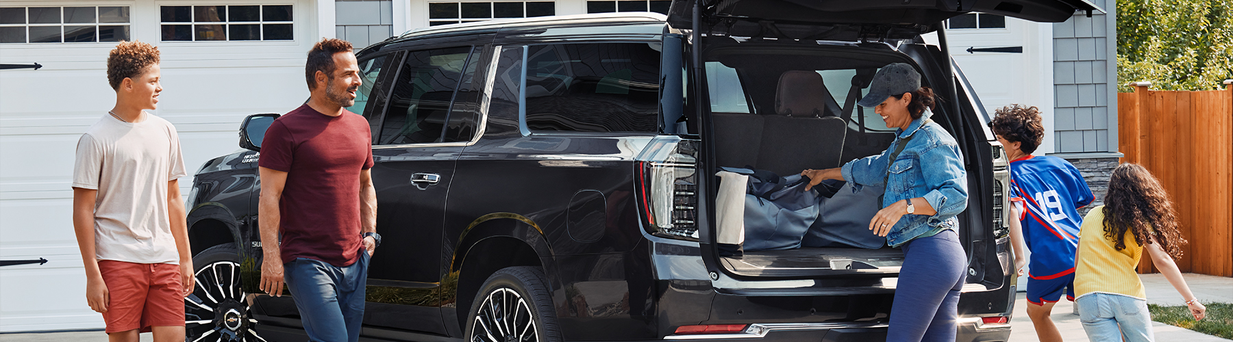 2025 Chevrolet Suburban High Country parked in house driveway with rear liftgate open with family outside of vehicle